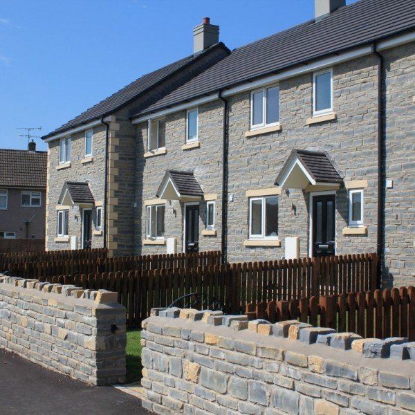Row of new gray stone houses with black doors, white window frames, and low stone and wooden fences.