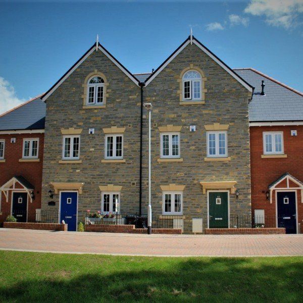 Row of modern townhouses with stone and brick facades; blue, green, and navy doors; clear blue sky.