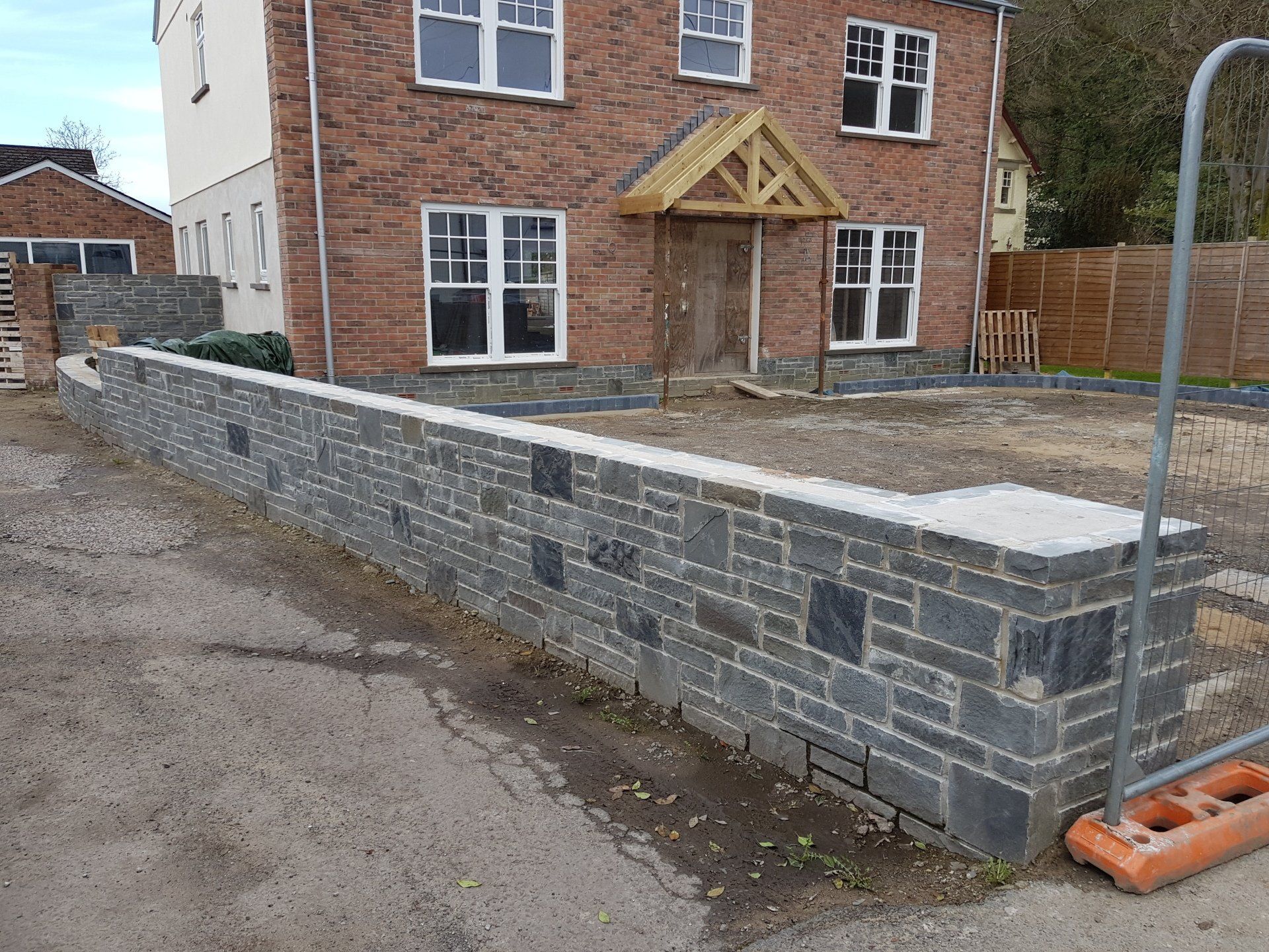 Gray stone wall in front of a brick house under construction.