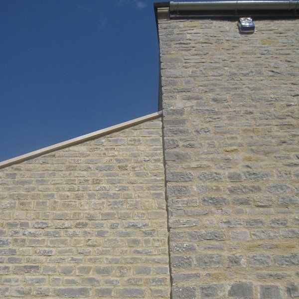 Stone building exterior against a blue sky, featuring a sloped roofline and a straight, vertical wall.