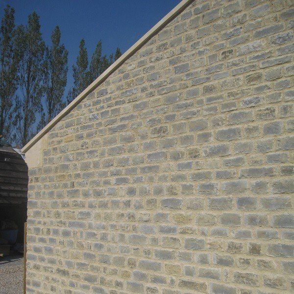 Stone brick wall, light-colored bricks, neutral mortar, with a beige border and blue sky in background.