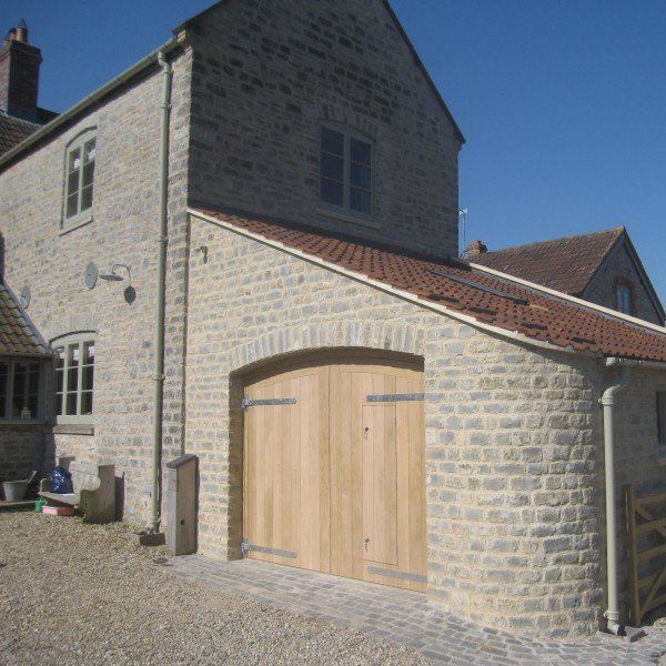 Stone house with arched wooden garage doors, red-tiled roof, and gravel driveway.