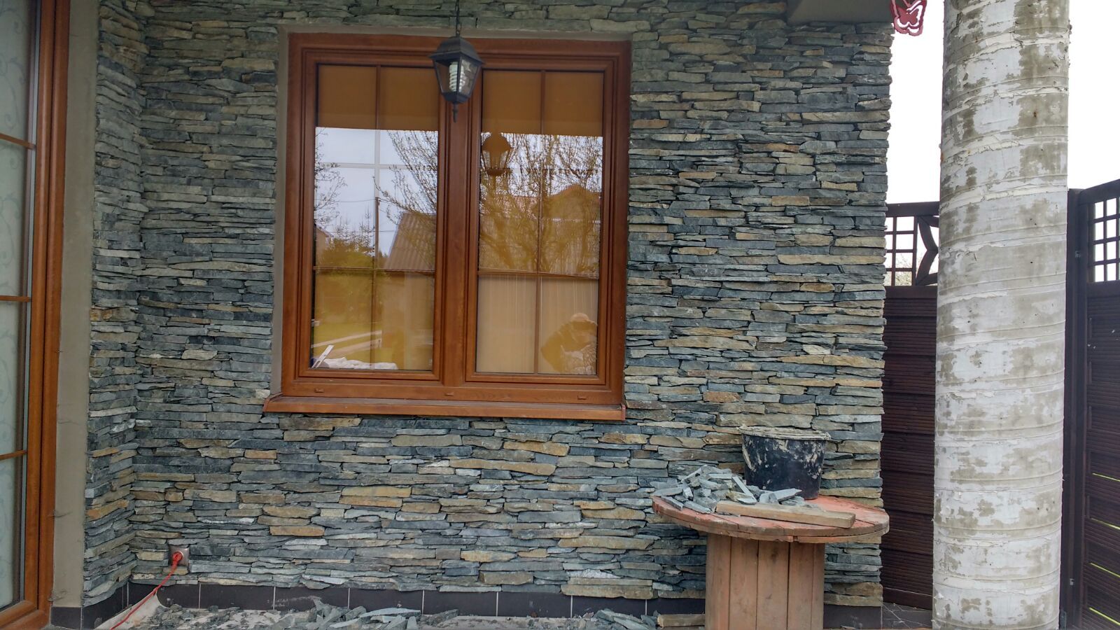 Window with brown frame, set in a stone-covered wall. Wooden cable reel table in the foreground.
