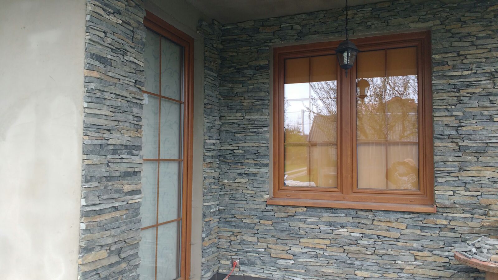 Exterior view of a building with a stone-covered wall, a brown wooden window, and a door.
