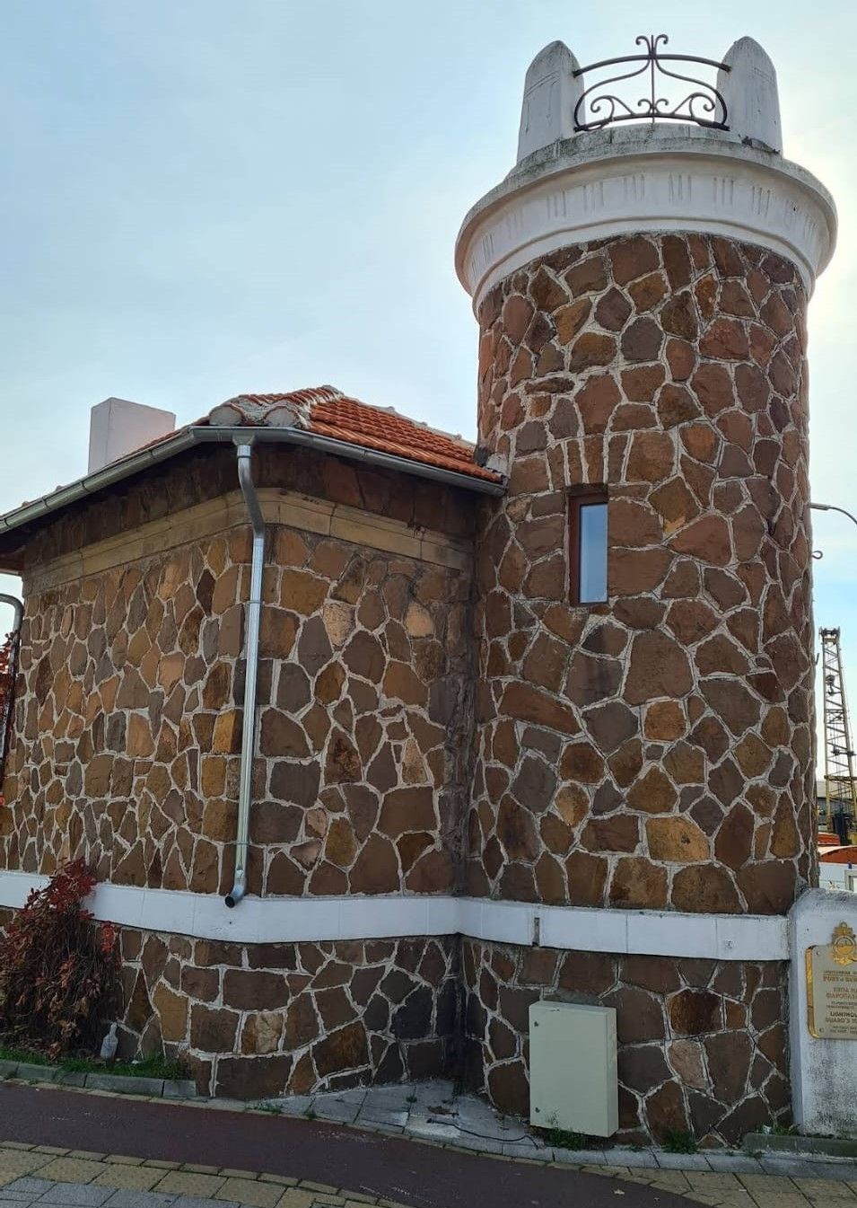 Stone building with a cylindrical tower and red-tiled roof under a cloudy sky.