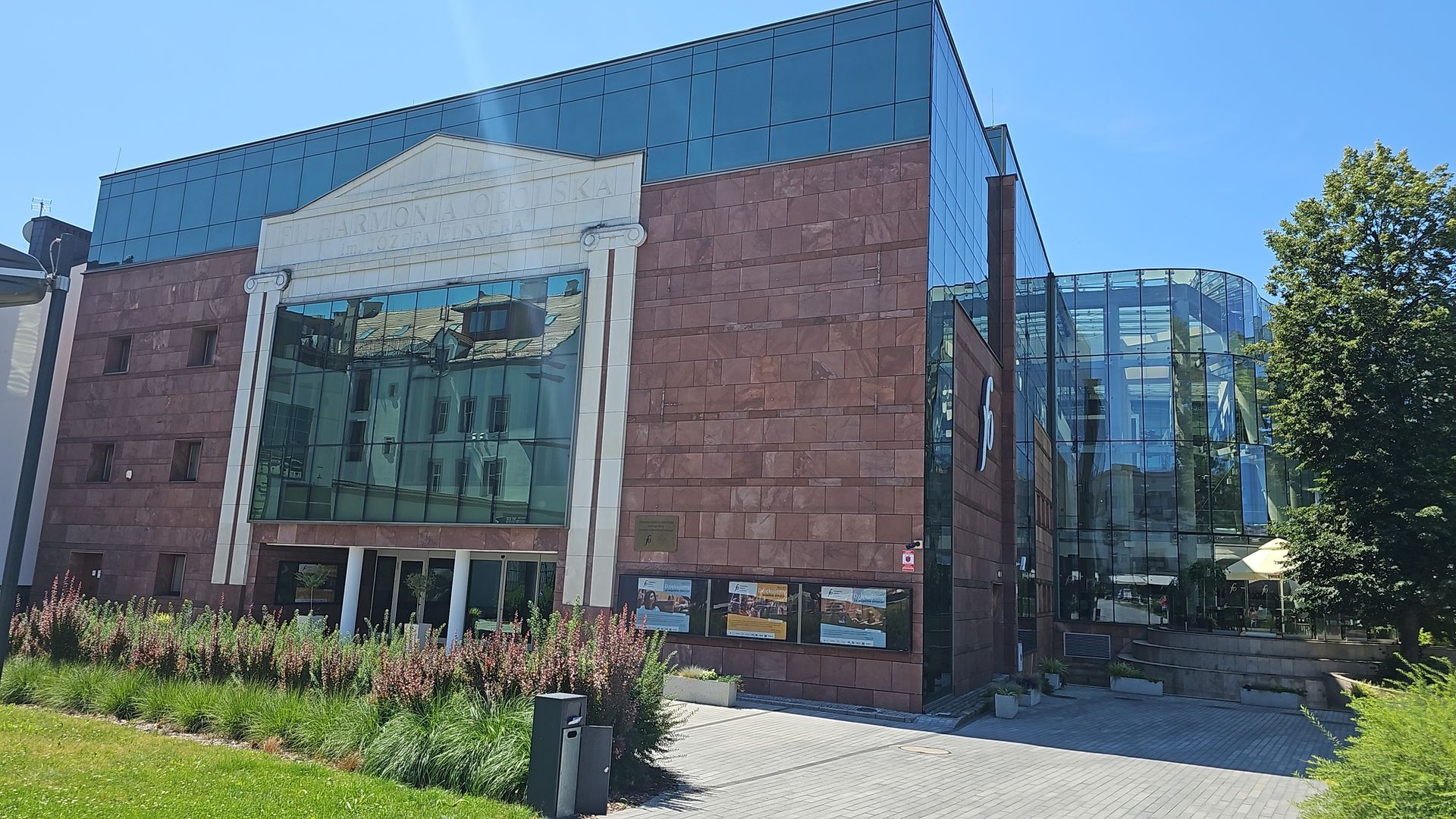 Red stone building with glass facade, likely a theater or cultural center, on a sunny day.