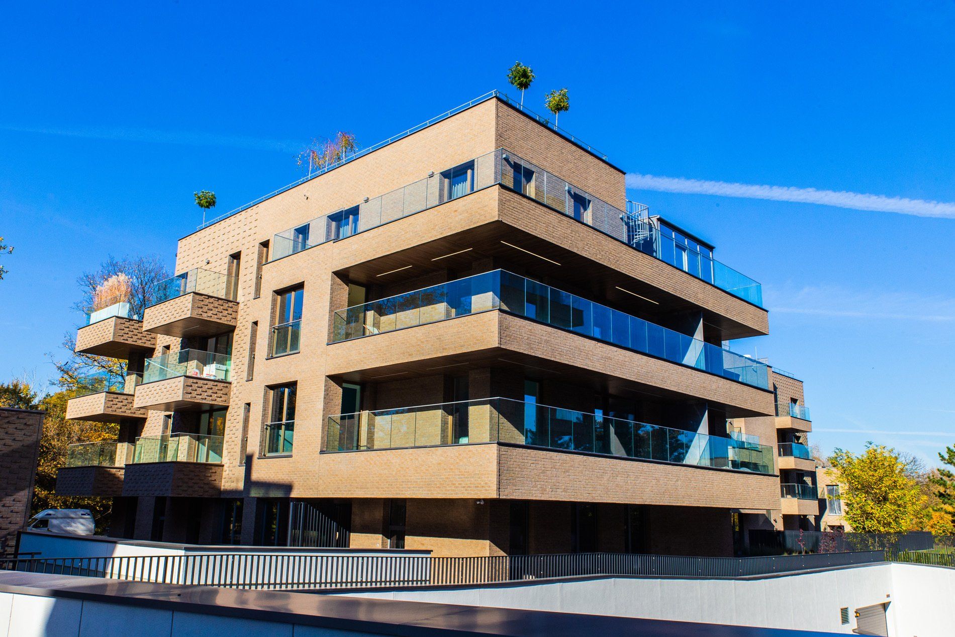 Modern brick apartment building with glass balconies, under a blue sky.