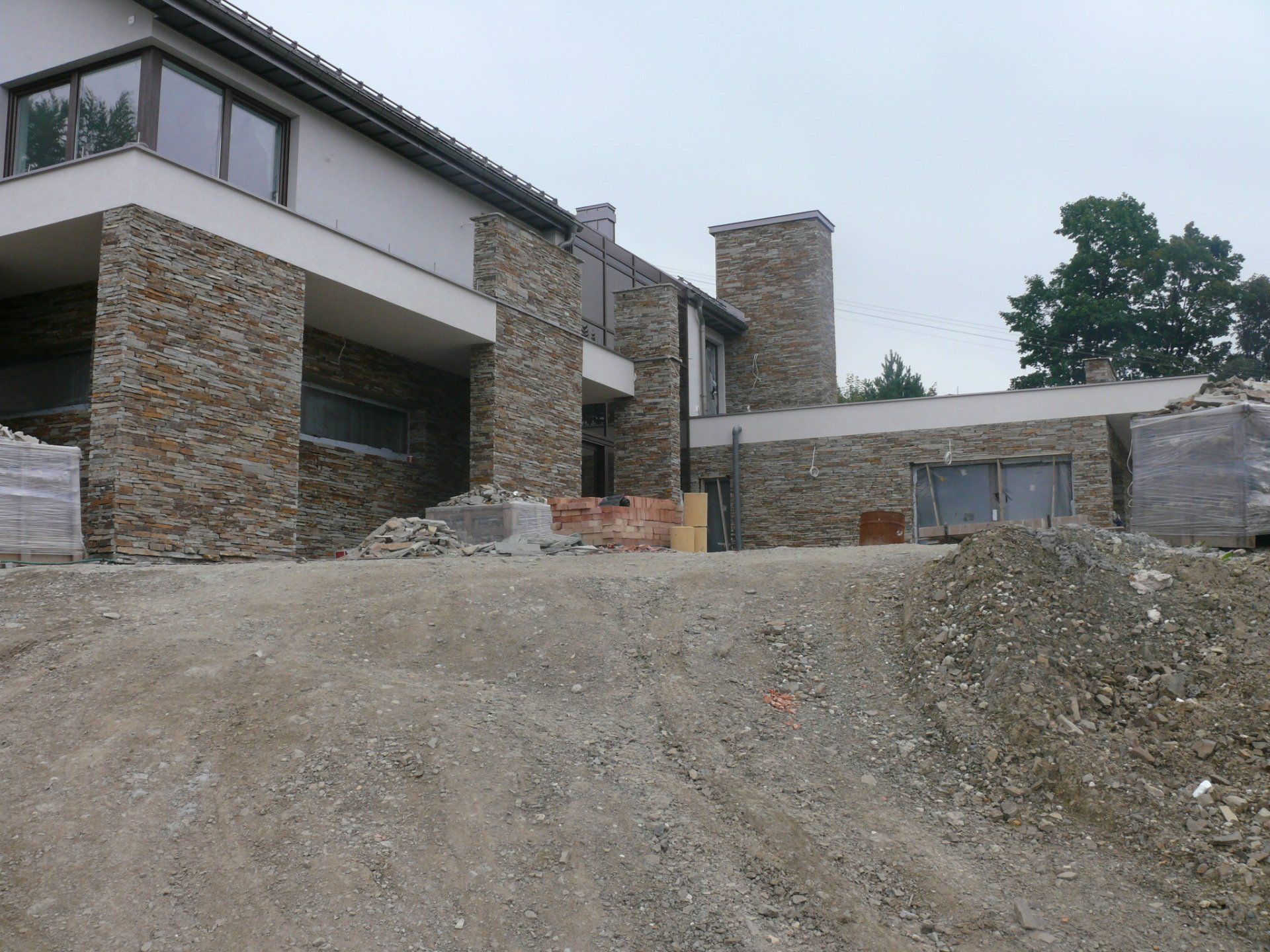 A two-story building under construction with stone facade and a mound of gravel in the foreground.