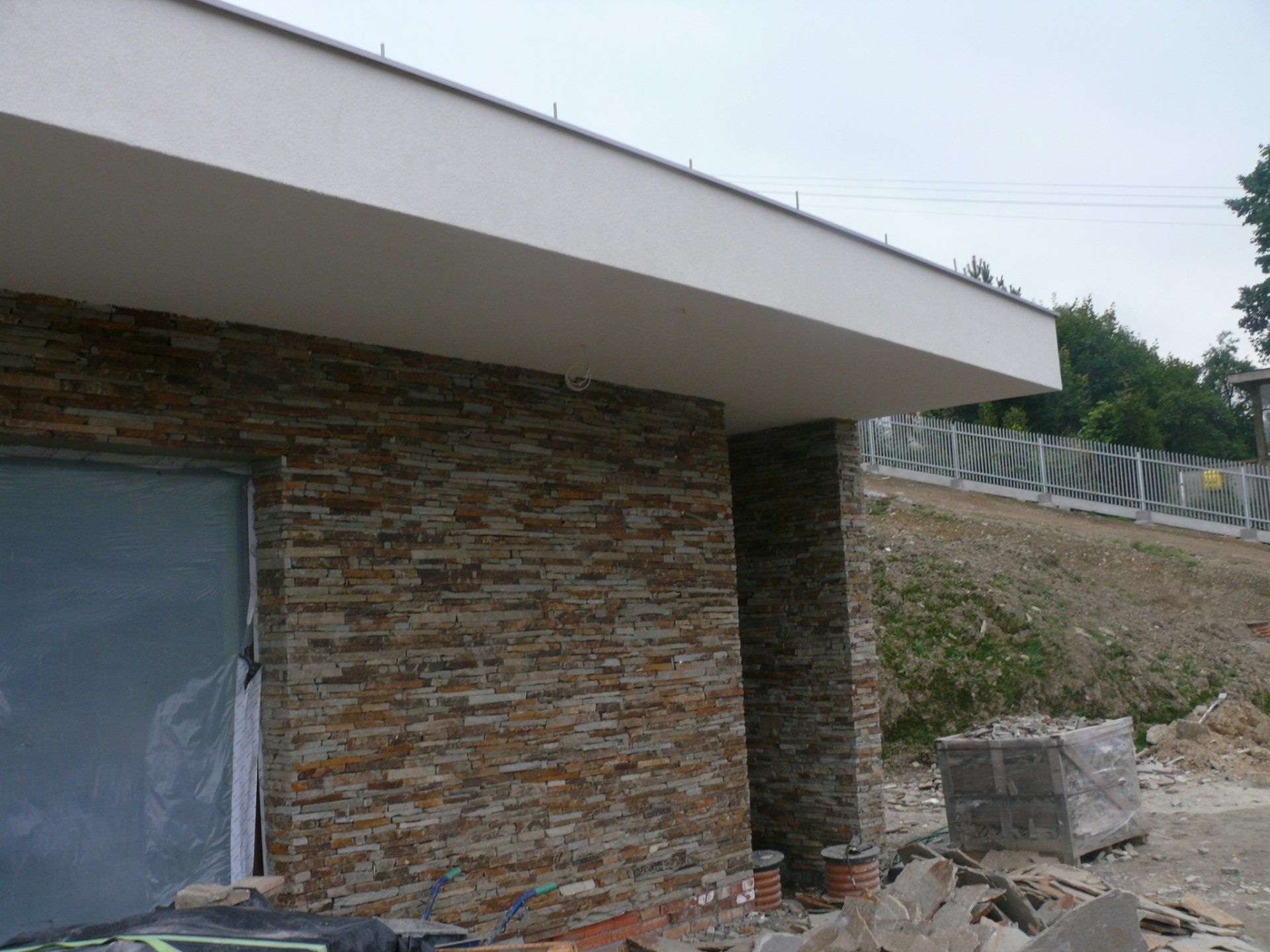 Stone-clad building exterior under construction, with a white roof overhang.