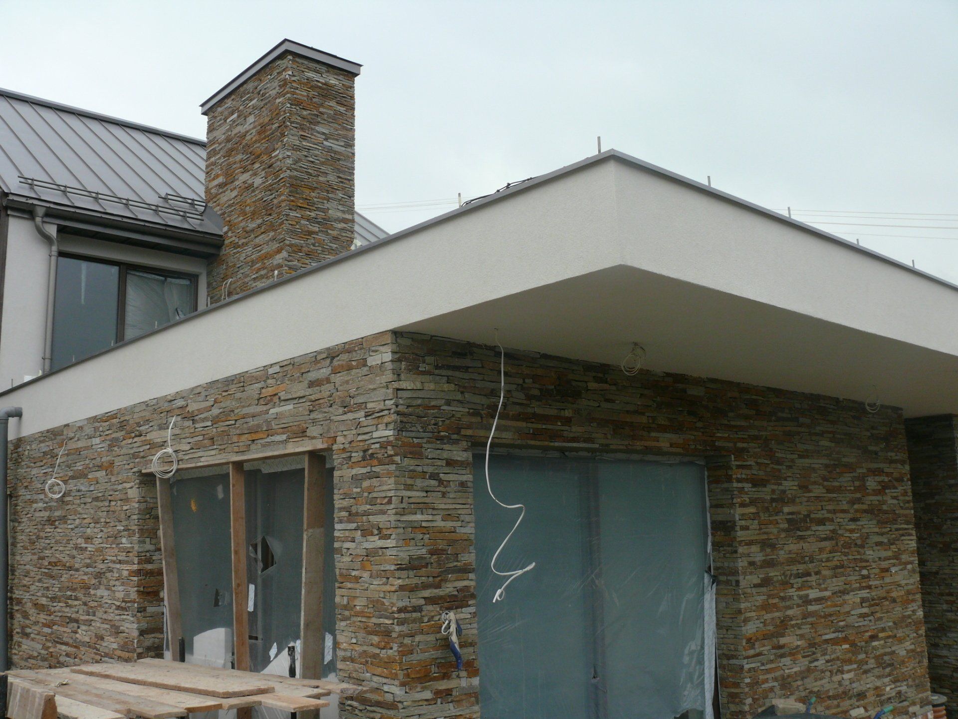 Exterior of a house with stone veneer siding, chimney, and metal roof under construction.