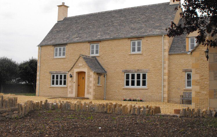 Beige stone house with gray slate roof and gravel yard.