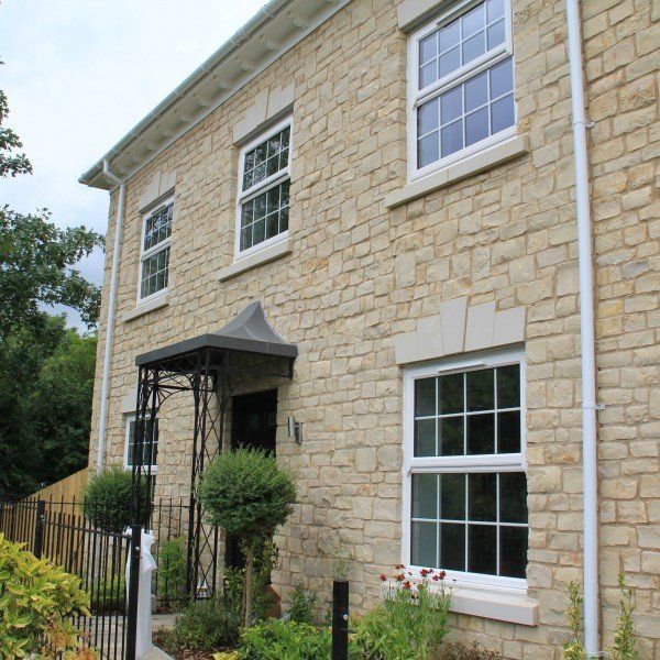 Stone-clad house with white-framed windows, a black wrought-iron awning, and a small garden.