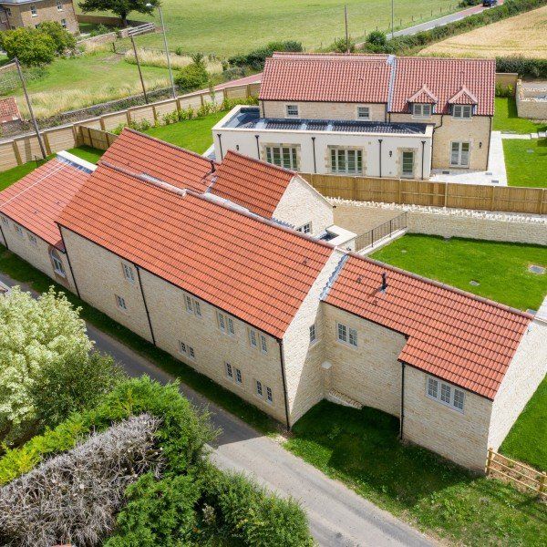 Aerial view of light-colored stone buildings with red tile roofs surrounded by green lawns and fields.