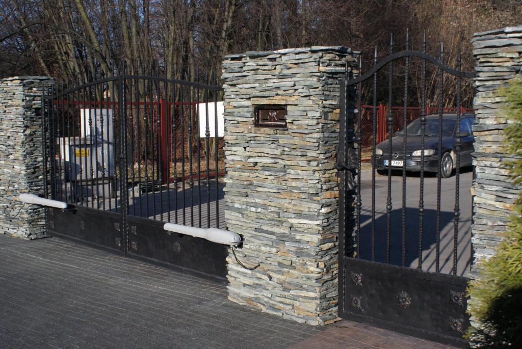 Black wrought iron gates between stone pillars; a car is visible beyond.
