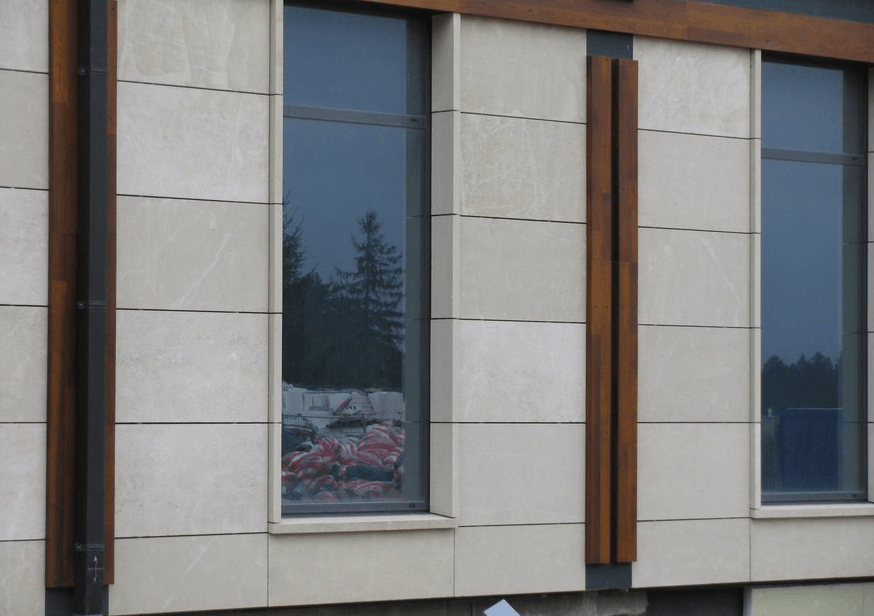 Exterior of a building with tall windows and beige stone facade, with dark wood accents.