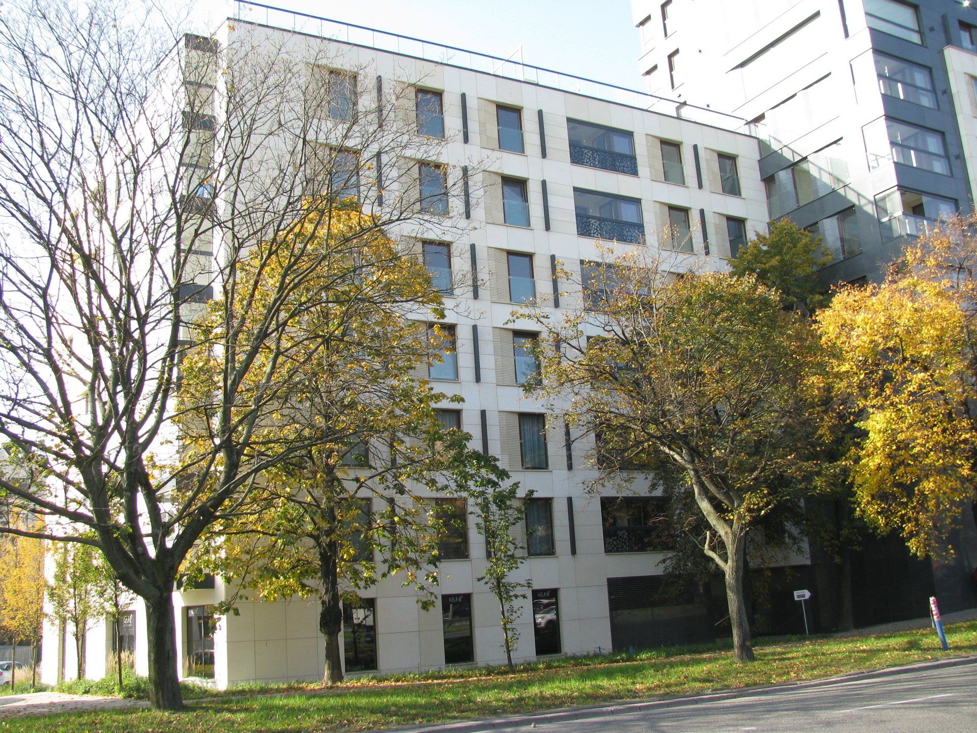 White apartment building with trees in front, under a blue sky.