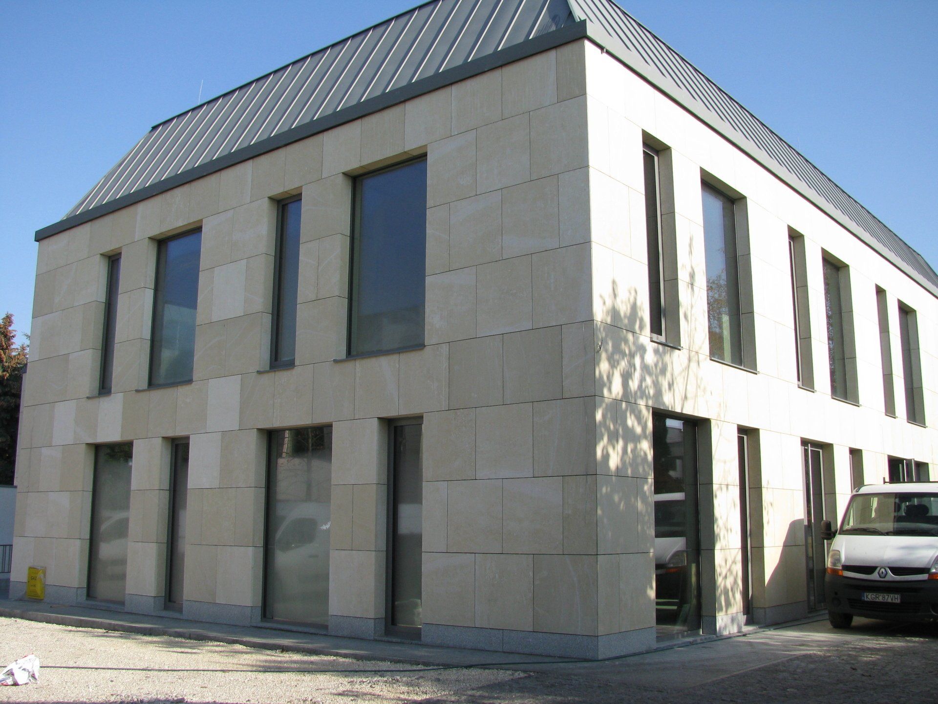 Two-story modern building with stone facade, dark-framed windows, and metal roof.