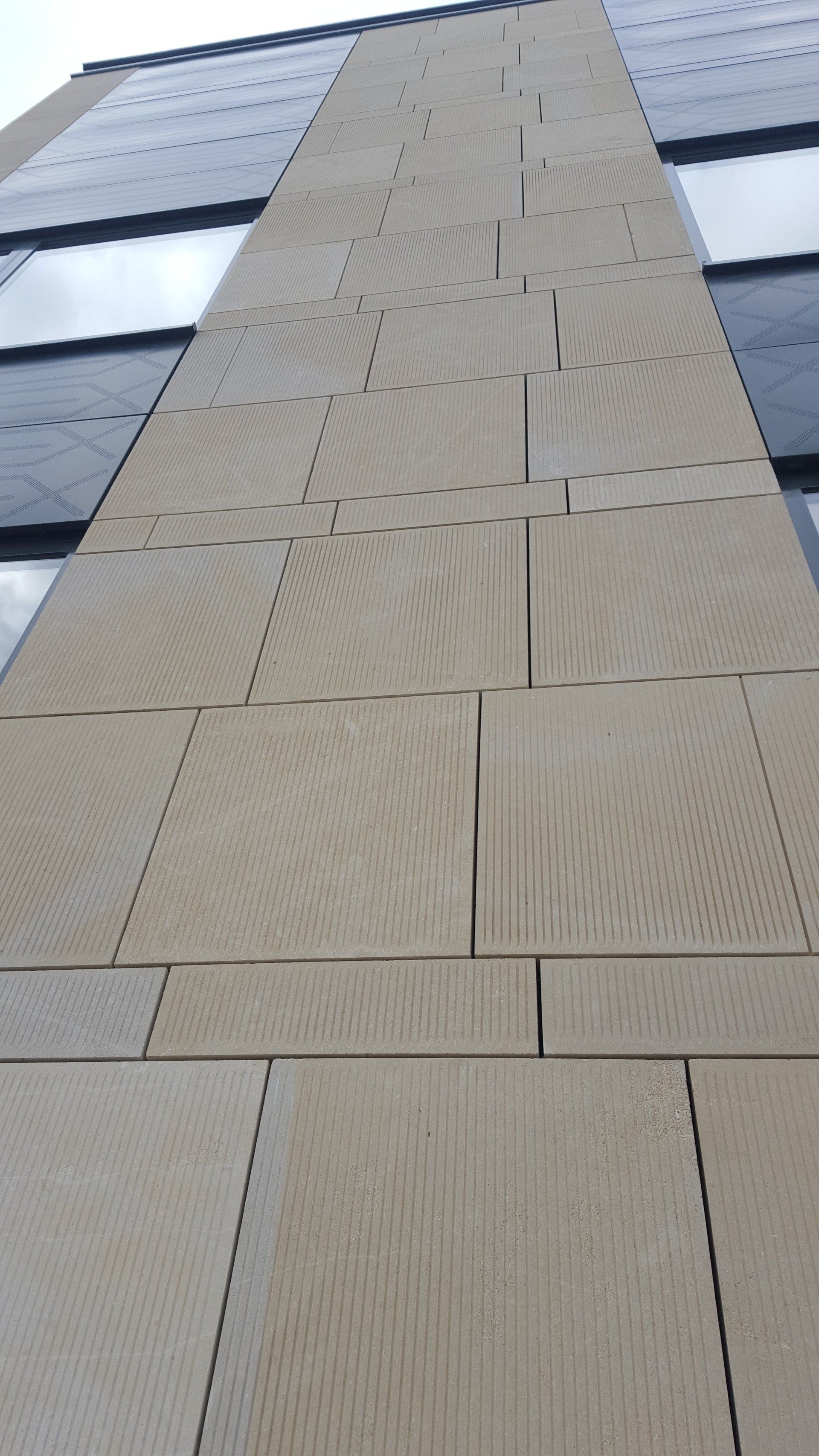Tan stone facade of a tall building with glass windows, viewed from below.