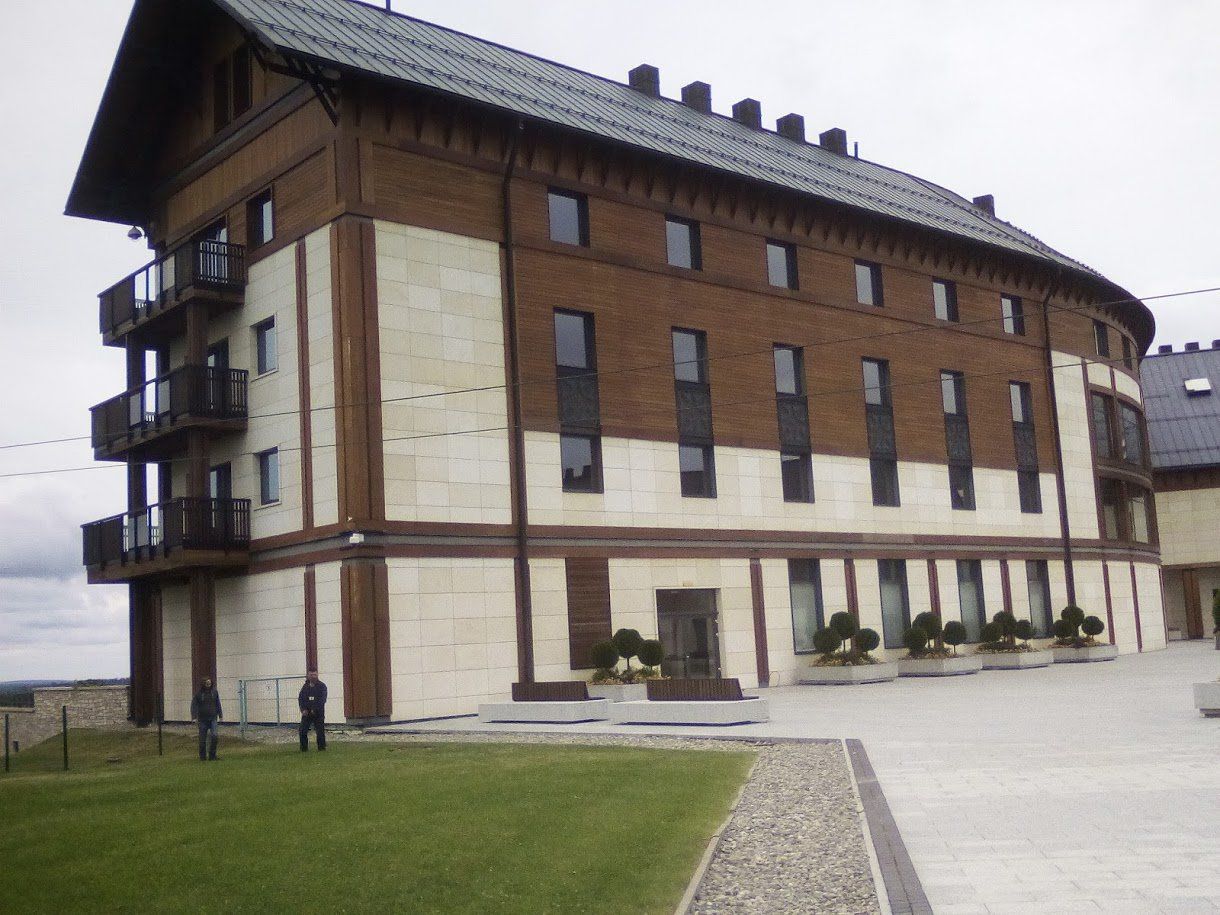A multi-story building with a brown and white exterior, two people standing in front on a cloudy day.