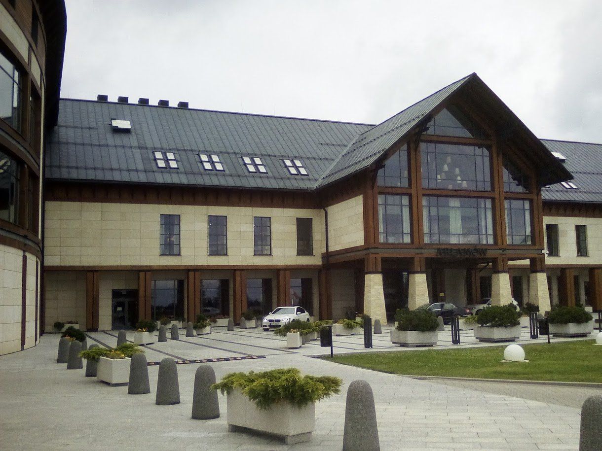 Hotel exterior with large glass windows and wooden accents, gray roof, stone facade, overcast sky.
