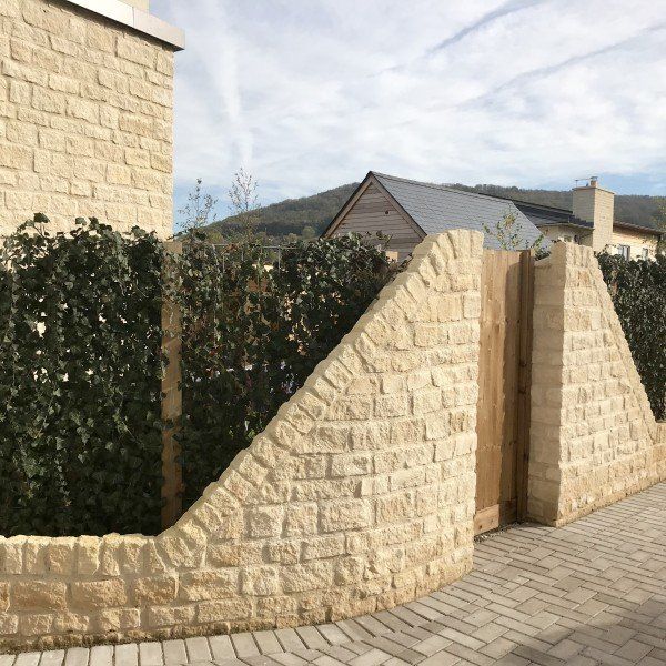 Stone wall with wooden gate and green hedge, set on a brick path.
