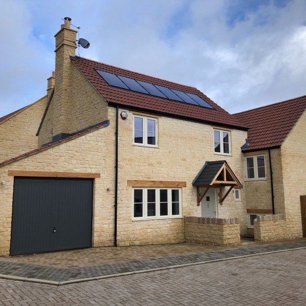 Two-story beige brick house with black garage door, solar panels on roof, and red tile roof.