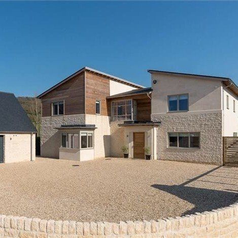Modern house with stone and wood exterior, gravel driveway, and clear blue sky.