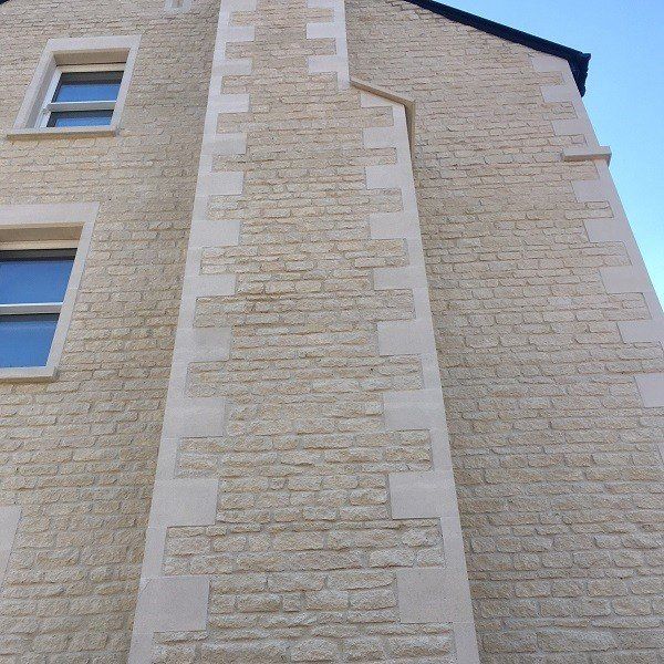 Beige stone building with light-colored stone accents on exterior chimney and around two windows.