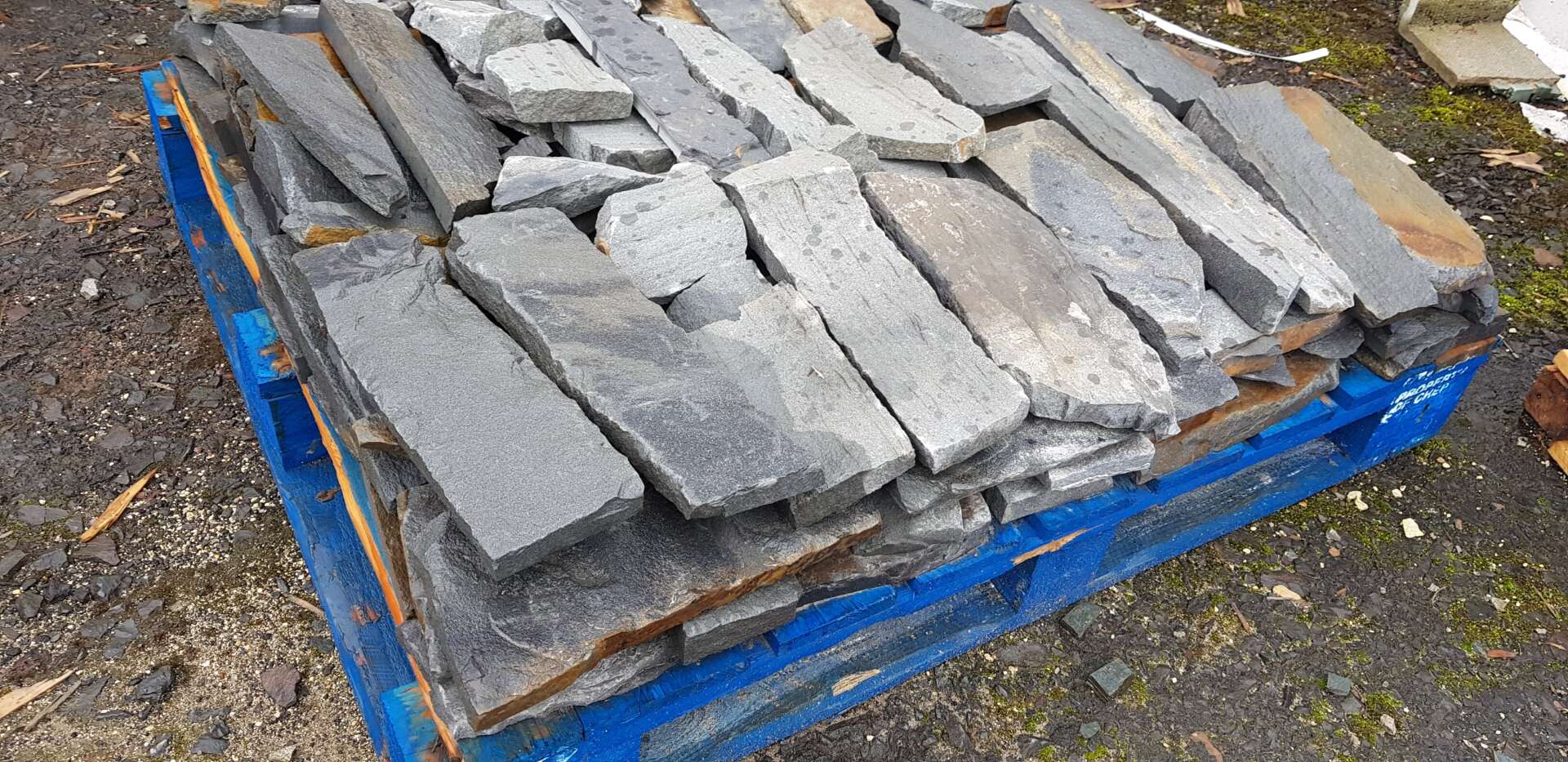Stack of gray stone tiles on a blue pallet, outdoors.