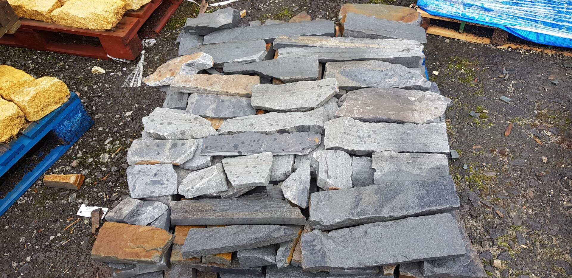 Stack of grey and tan rectangular stones, likely for landscaping, with wooden pallets visible.