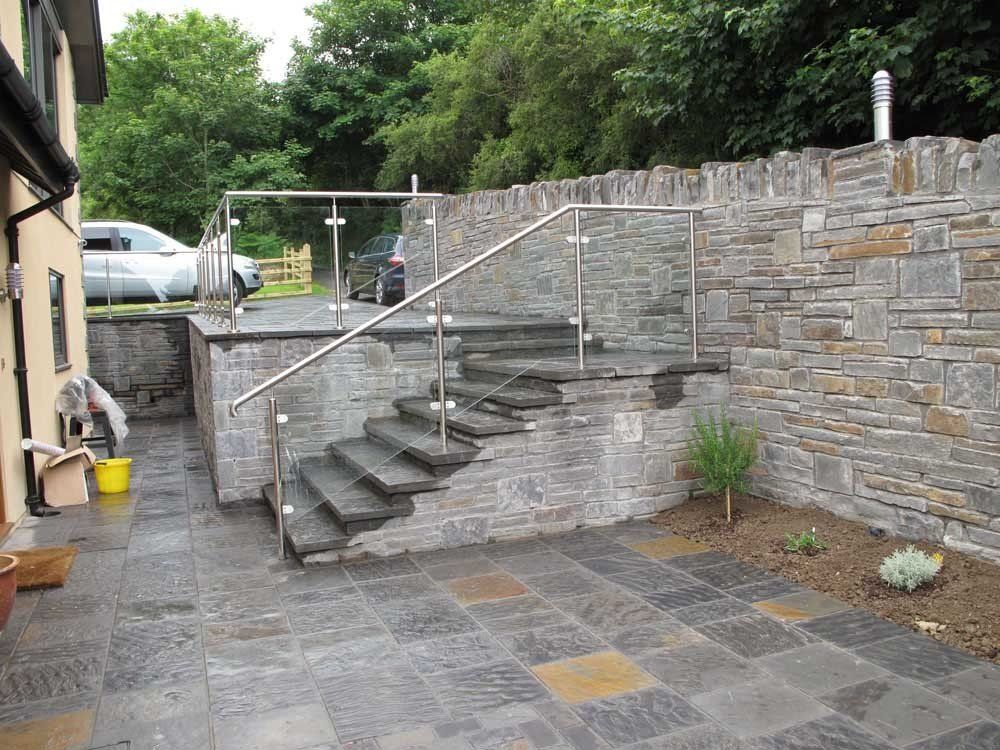 Exterior stone steps leading up to a platform with glass railings. Paved patio area.