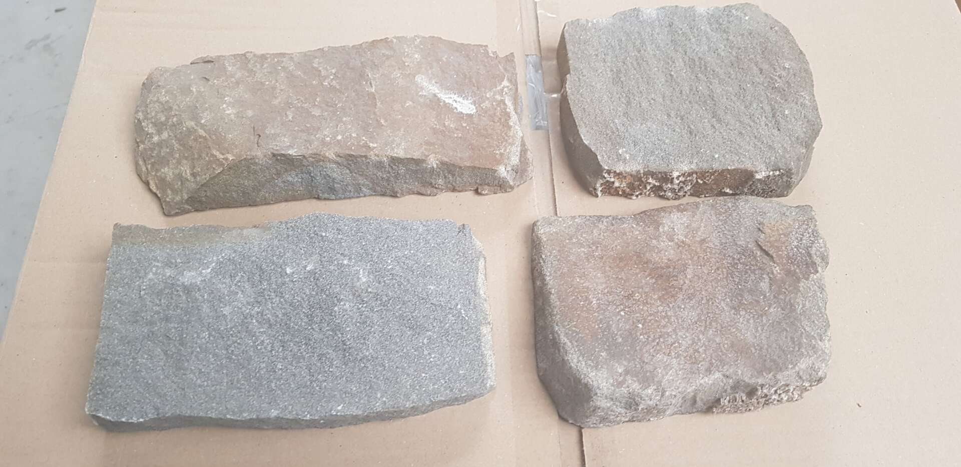 Four irregularly shaped, light-colored stone pavers arranged on a tan surface.