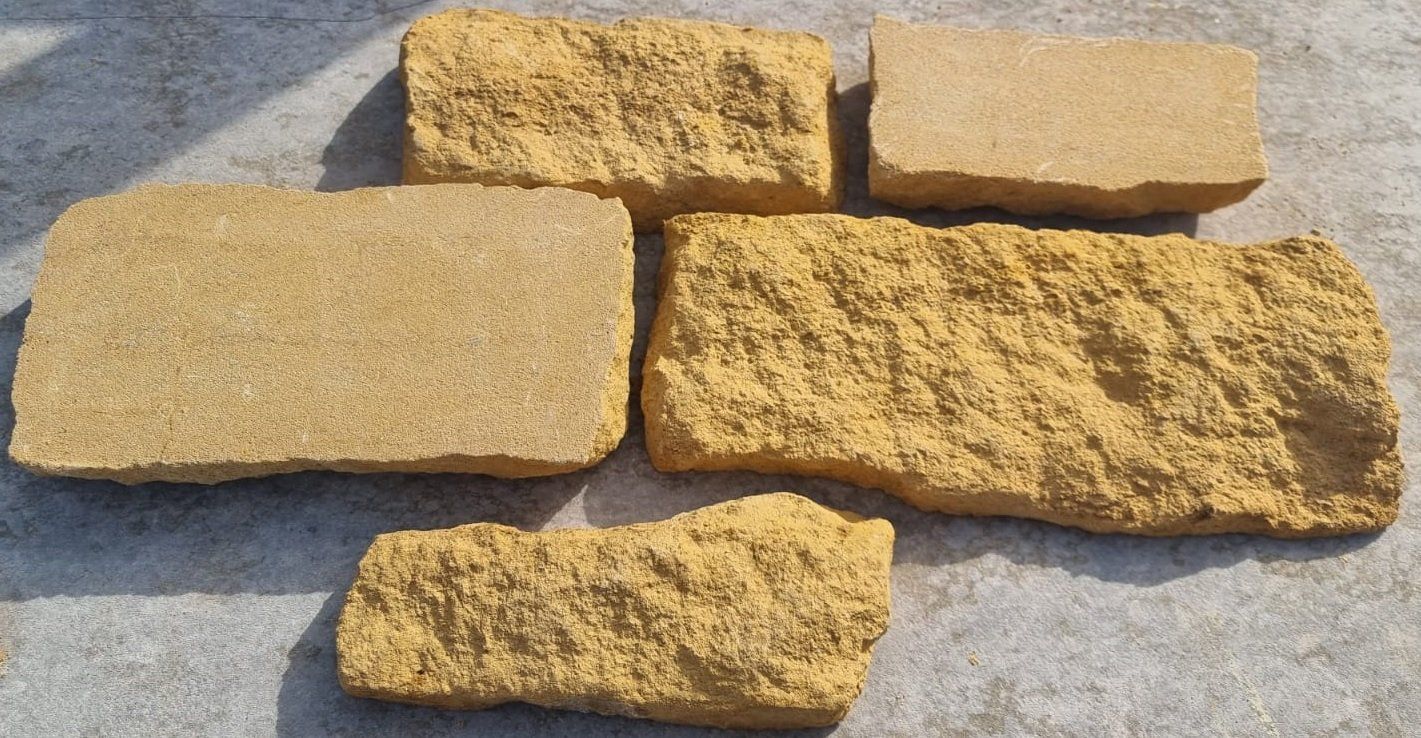 Six irregularly shaped, tan-colored bricks on a gray surface, with varying textures.