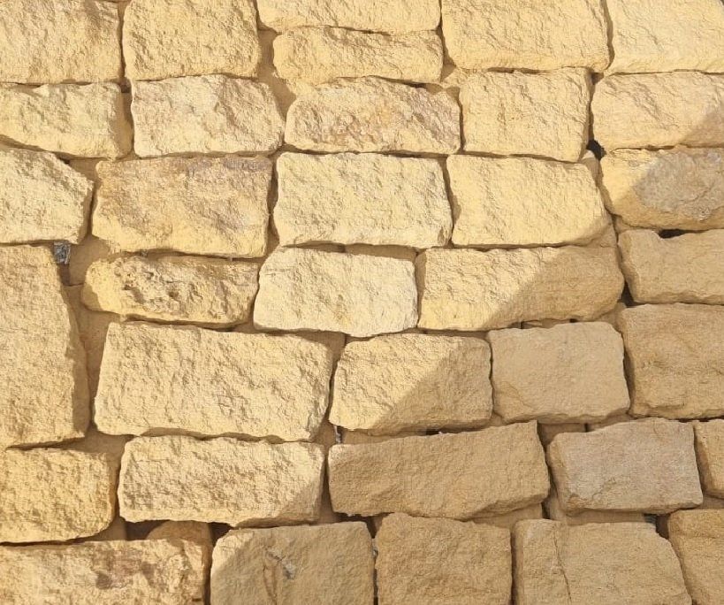Stone wall made of rough-cut, light tan blocks, with mortar.