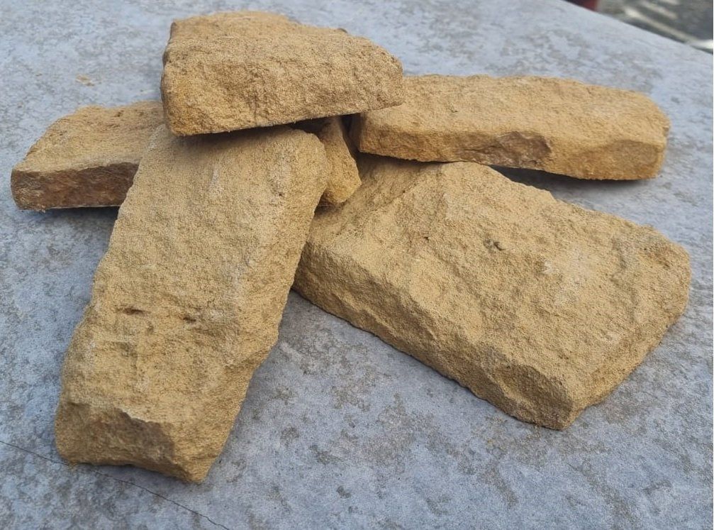 Pile of light brown rectangular stones on a grey surface.