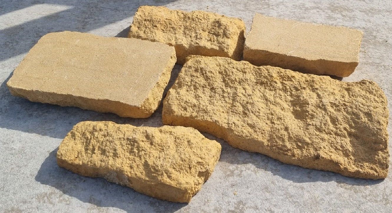 Five irregularly shaped, light-tan sandstone blocks arranged on a textured surface.
