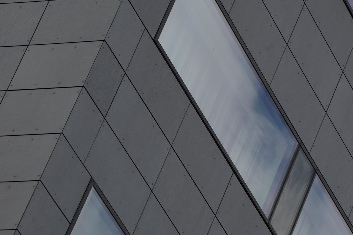 Gray modern building facade with rectangular panels and windows reflecting the sky.