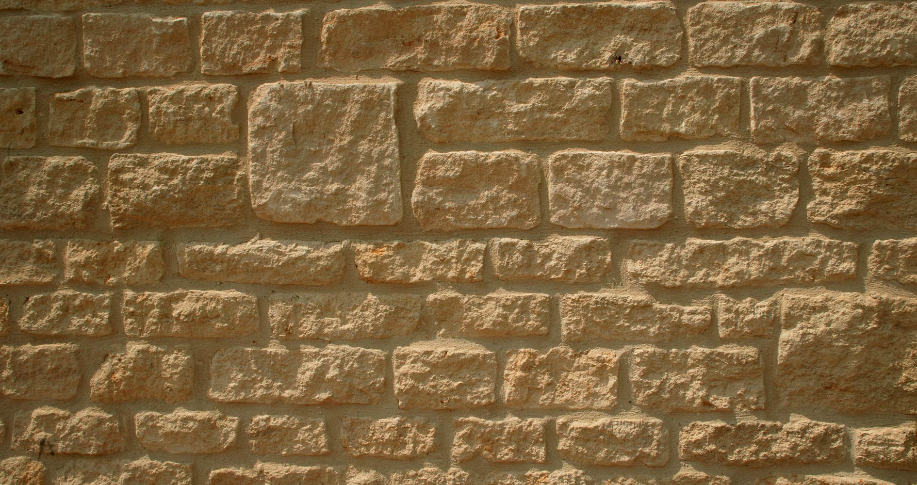 Rough, beige-colored stone brick wall with visible mortar.