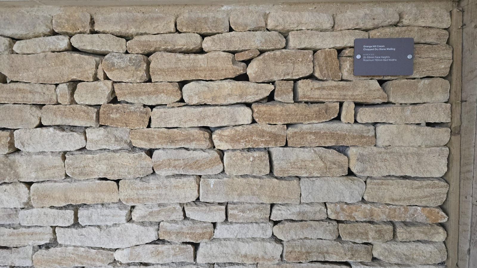 Stone wall with rectangular, tan-colored stones; a small sign is affixed.