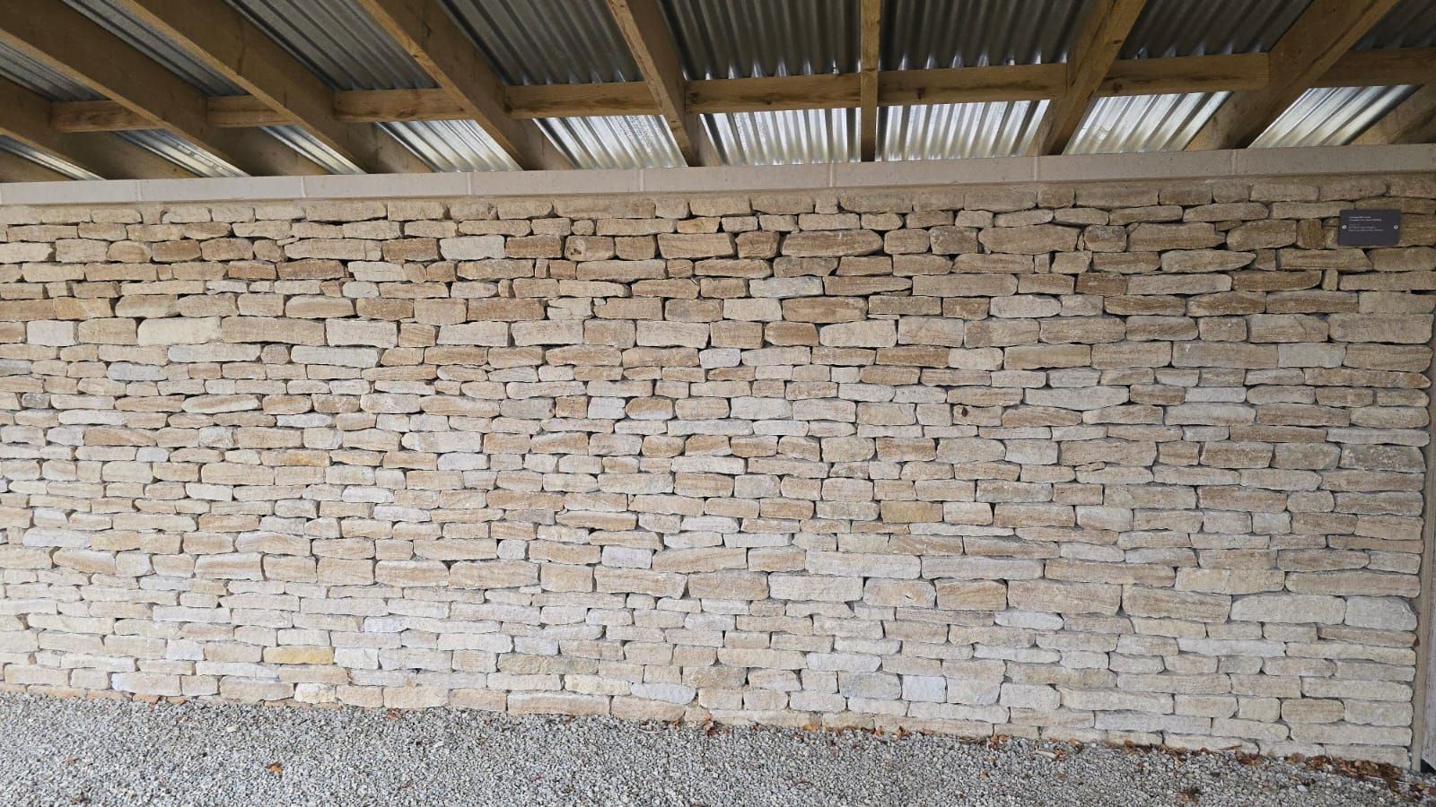 Stone block wall under a corrugated metal roof. Gravel ground.