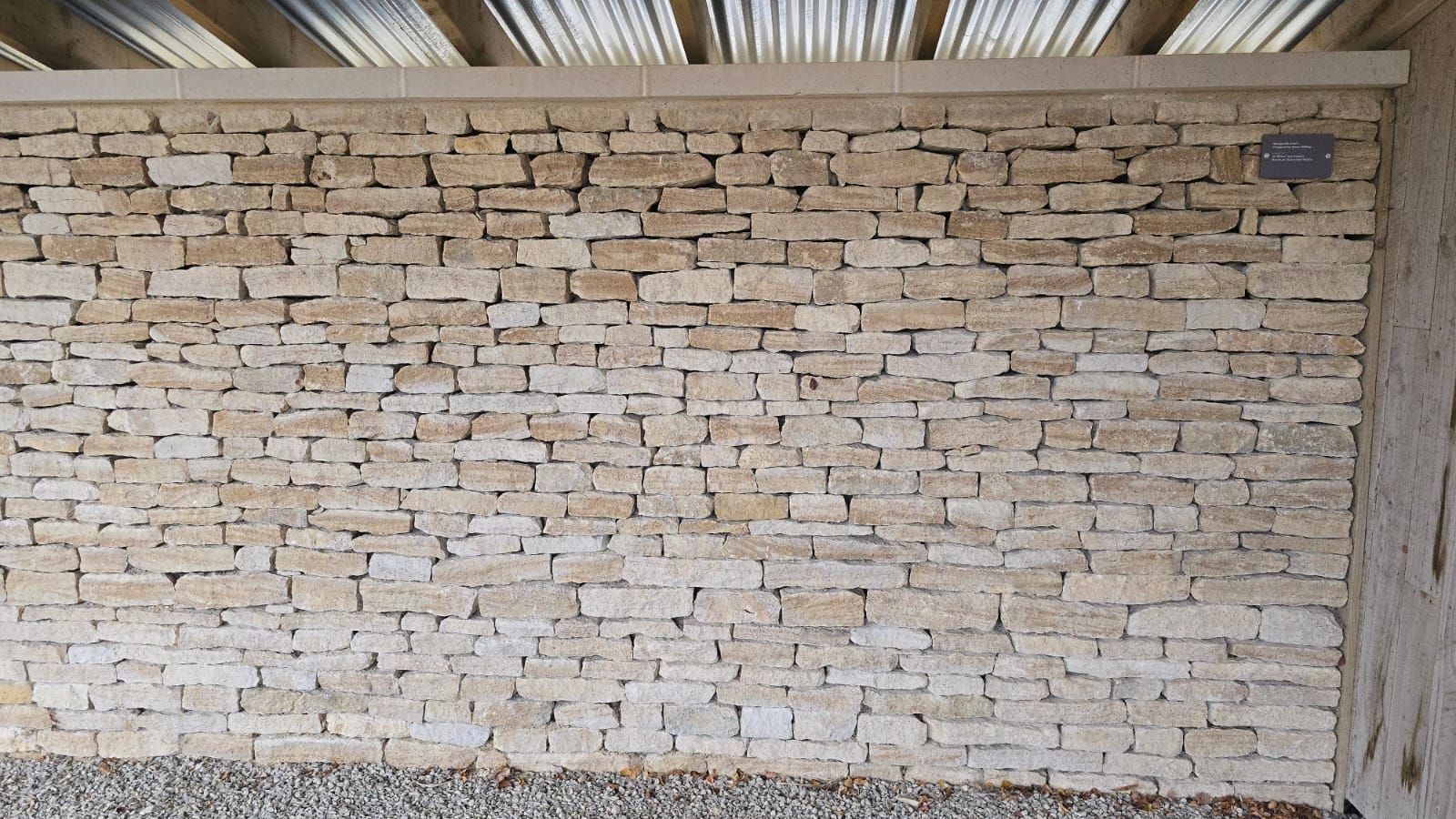 Stone wall with small, rectangular blocks under a corrugated metal roof.