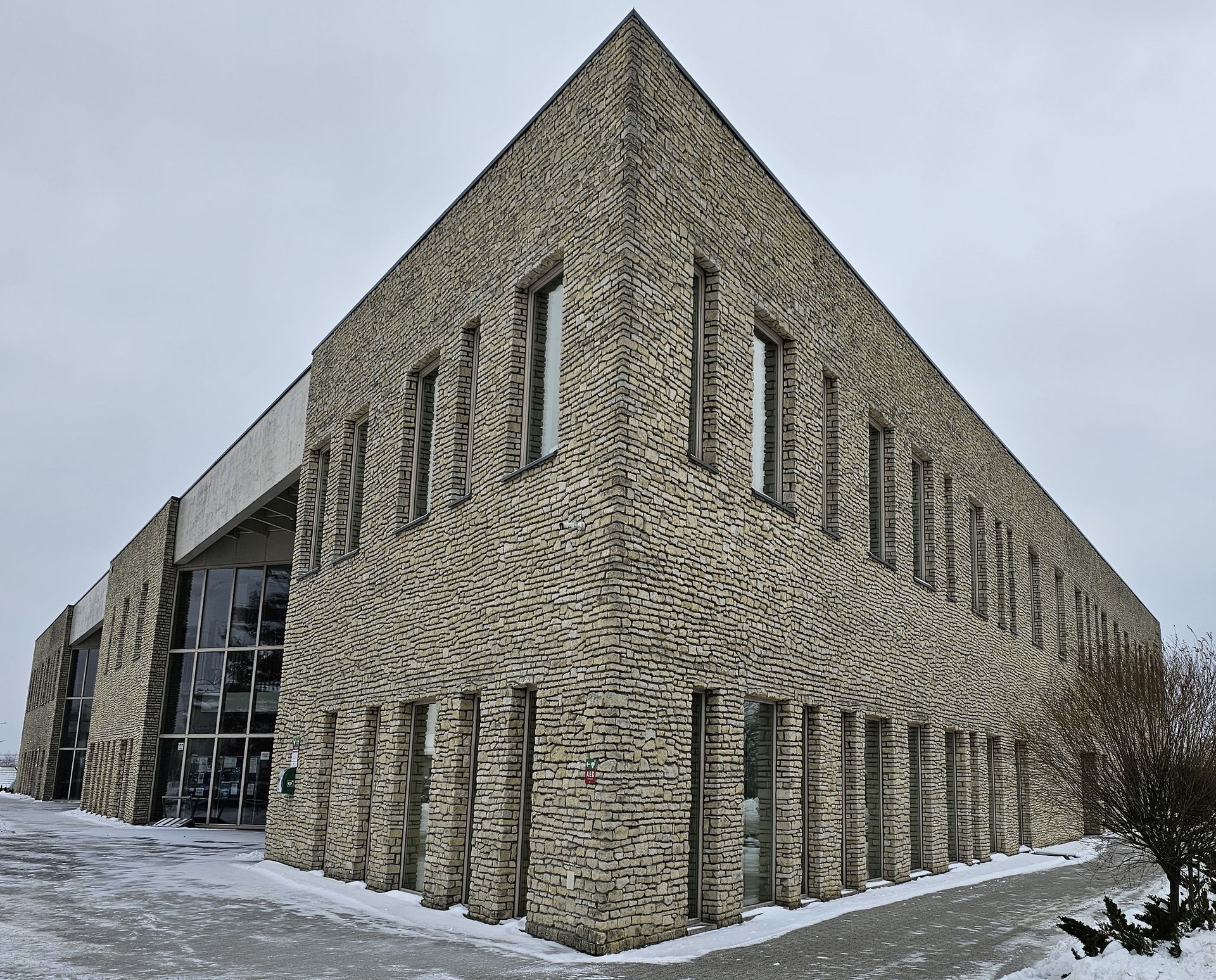 Corner view of a modern building with a textured stone facade, windows, and snow-covered ground.