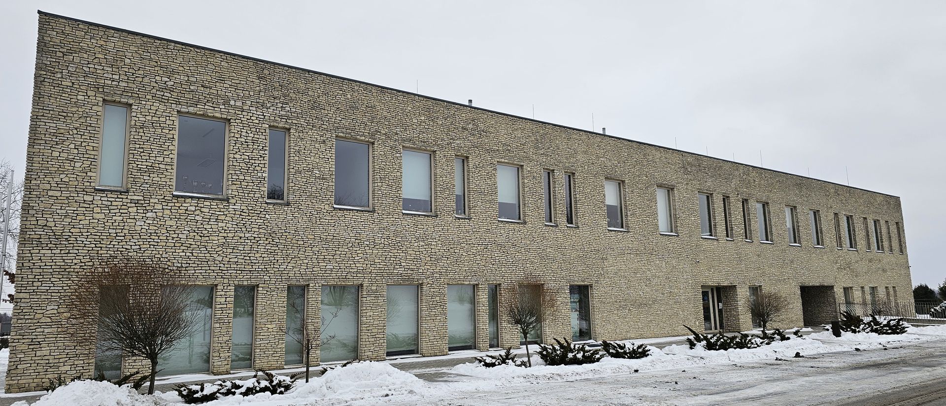 A long, two-story building with many windows, brick exterior, and snow on the ground.
