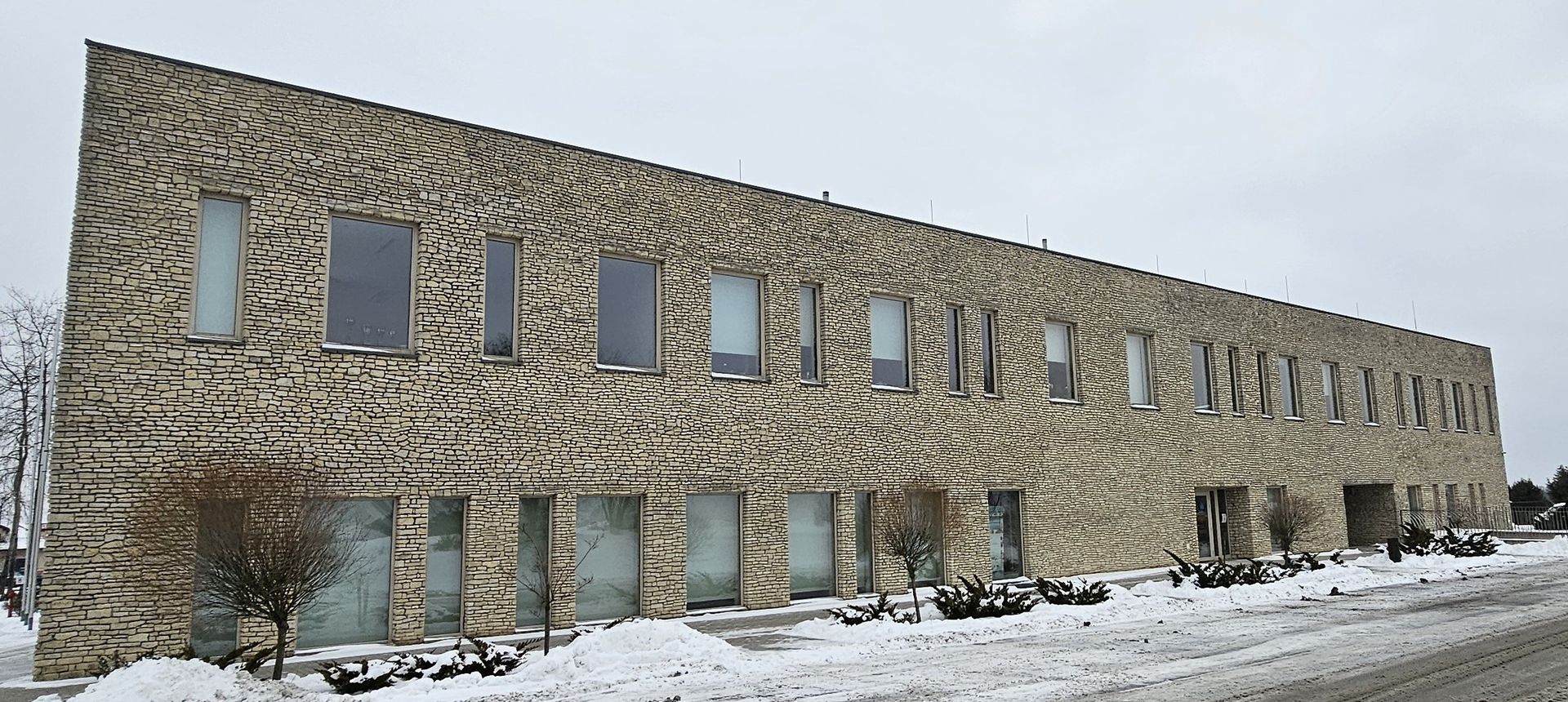 Brick building with many windows, snow on the ground in a winter setting.