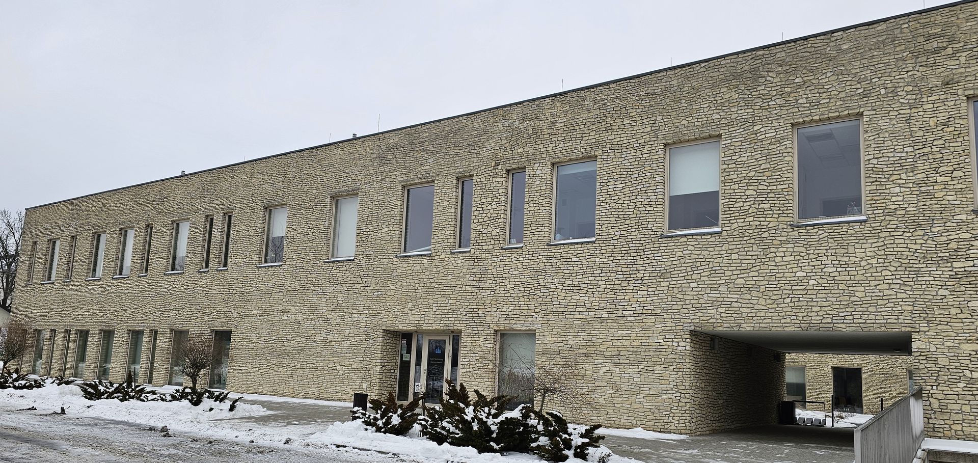 A long, stone building with snow on the ground in front of it under a cloudy sky.