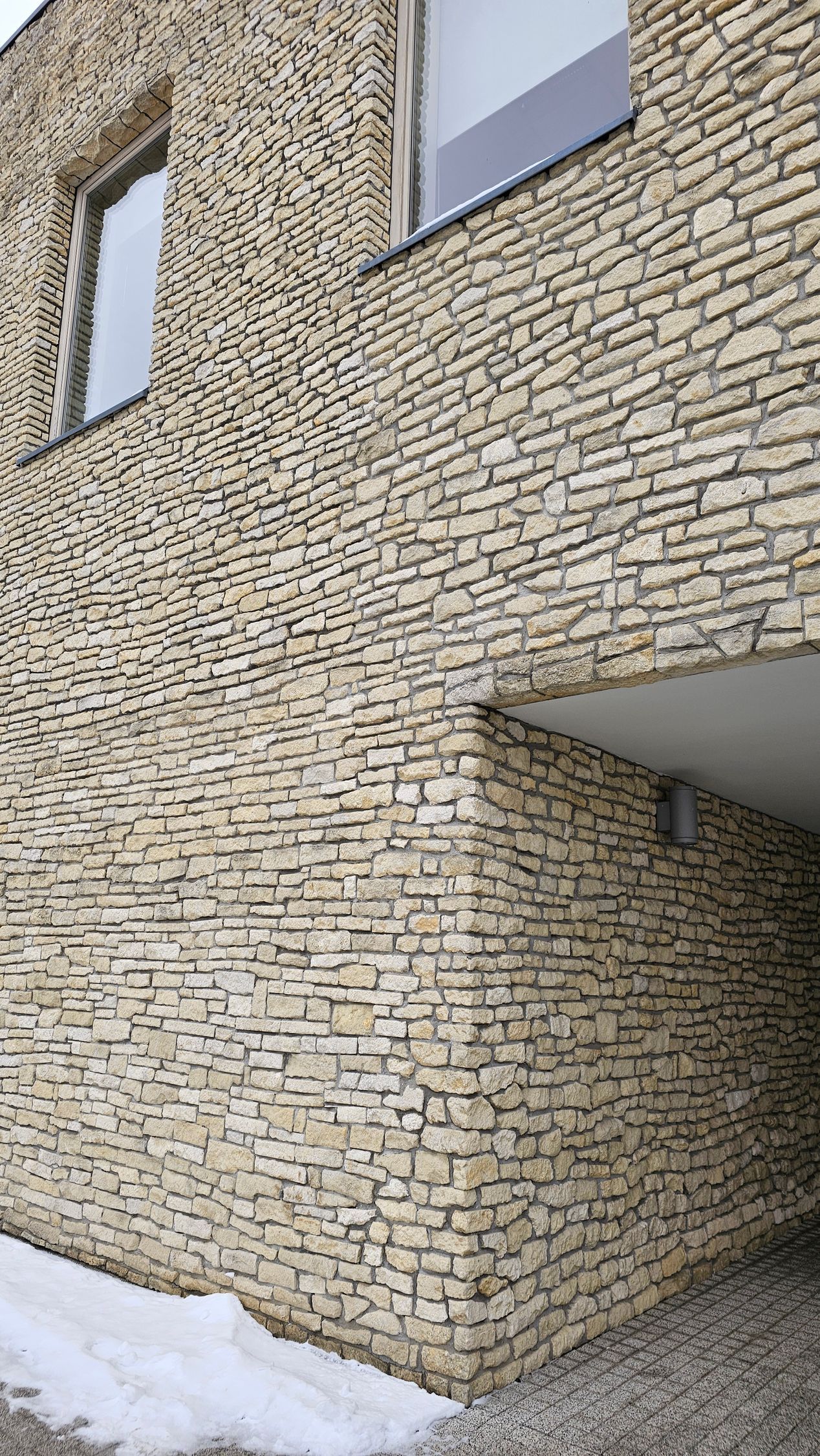Building exterior with light stone facade, windows, and an overhang.