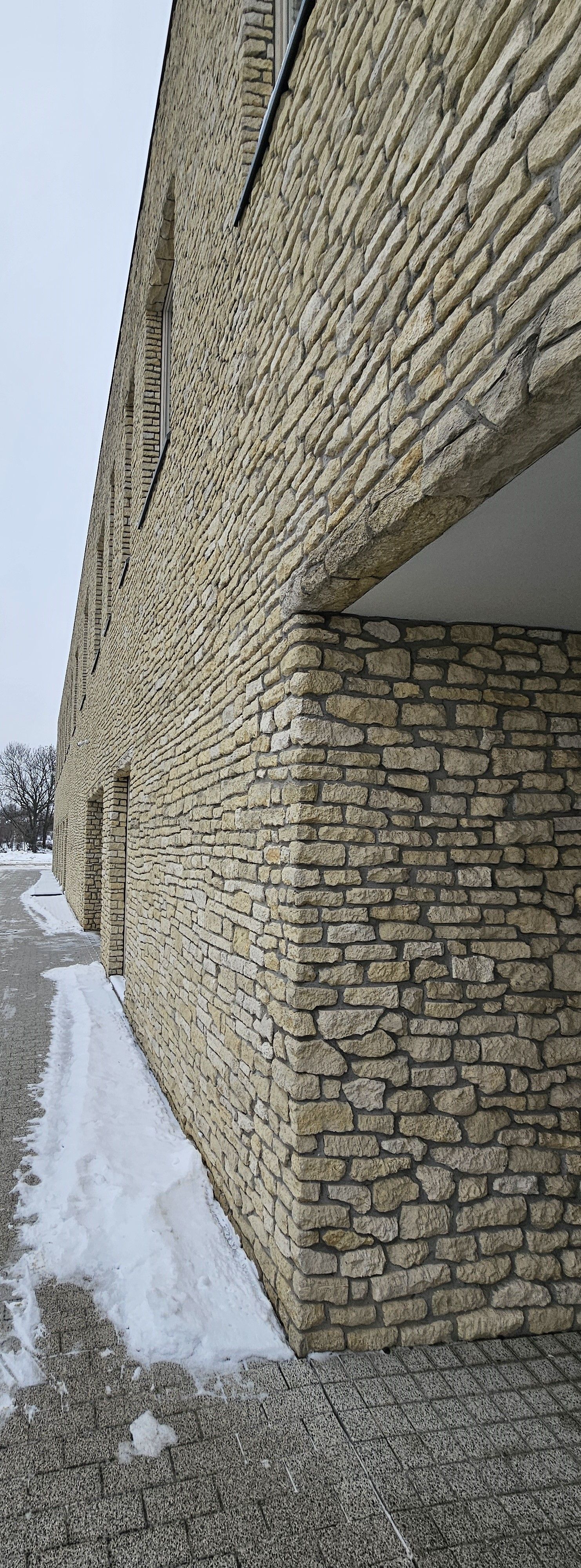 Stone-clad building corner with an overhang and snow-covered walkway.
