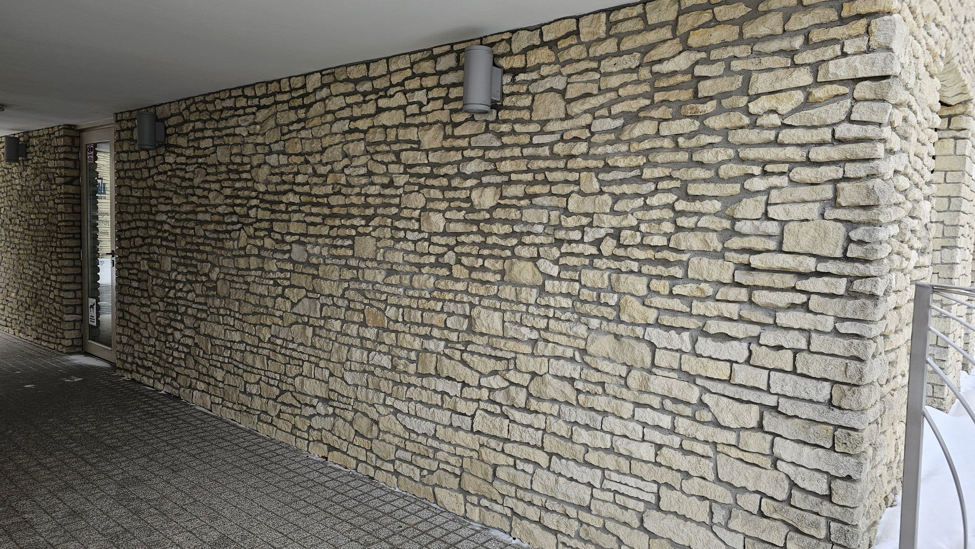Stone wall with light-colored, irregularly shaped blocks. Gray mortar. Two spotlights. Pebble flooring.