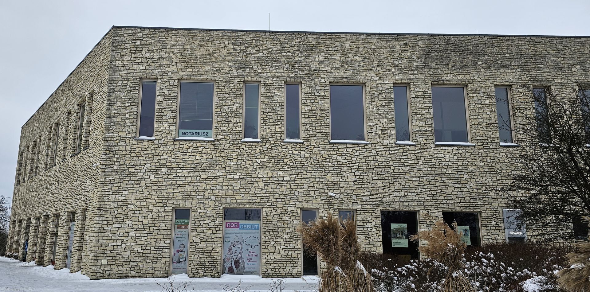 Stone-clad building with rectangular windows, snow-covered ground, and a cloudy sky.