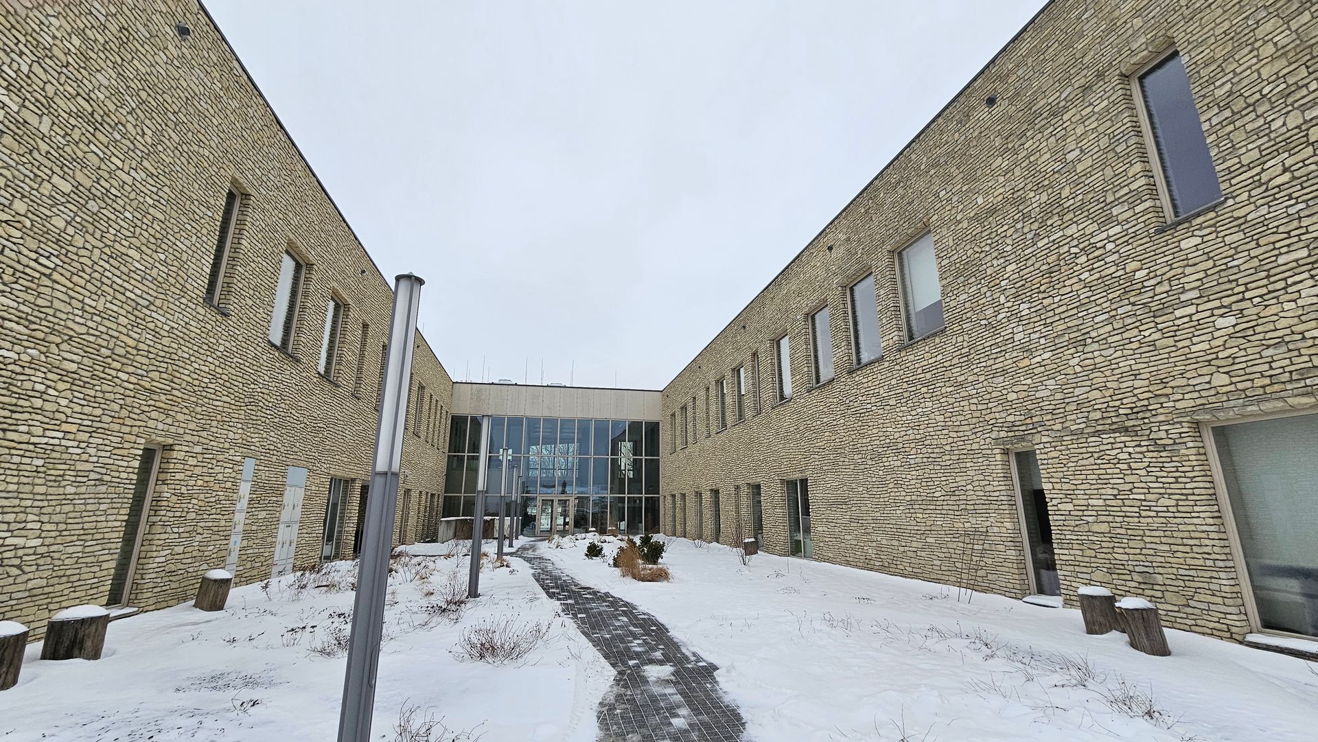 Snowy courtyard between two brick buildings. Glass entrance at the end.